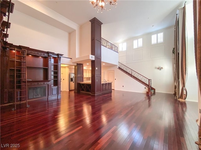 unfurnished living room featuring a high ceiling, ornamental molding, dark wood-type flooring, and a glass covered fireplace