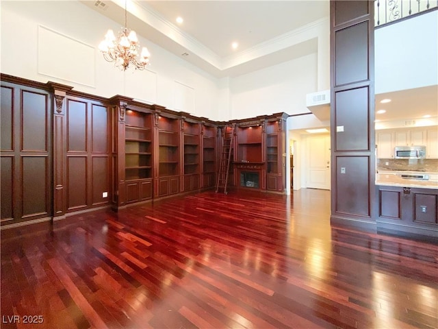 unfurnished living room with visible vents, dark wood-type flooring, a high ceiling, crown molding, and a chandelier