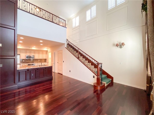 living area with a high ceiling, stairs, baseboards, and dark wood-type flooring