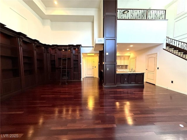 unfurnished living room with baseboards, visible vents, ornamental molding, dark wood-type flooring, and a high ceiling