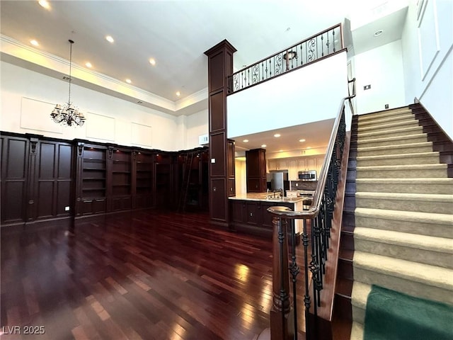 interior space featuring a raised ceiling, a high ceiling, dark wood-type flooring, ornamental molding, and stairs