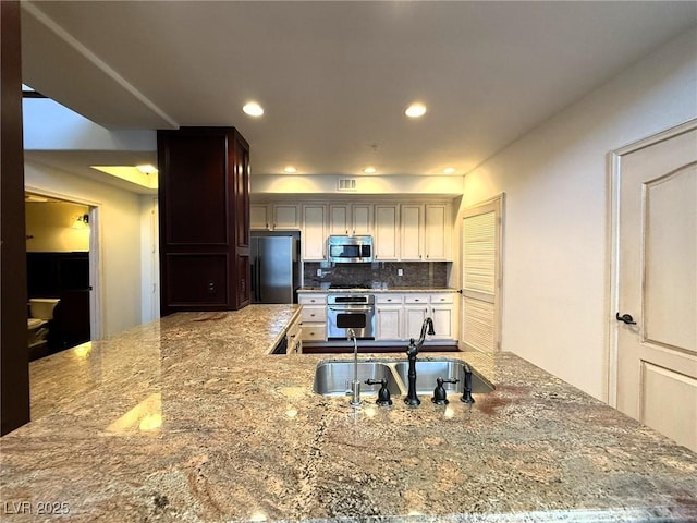 kitchen with stainless steel appliances, a sink, backsplash, and light stone counters