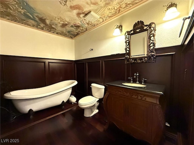 bathroom featuring a freestanding bath, toilet, wainscoting, vanity, and wood finished floors