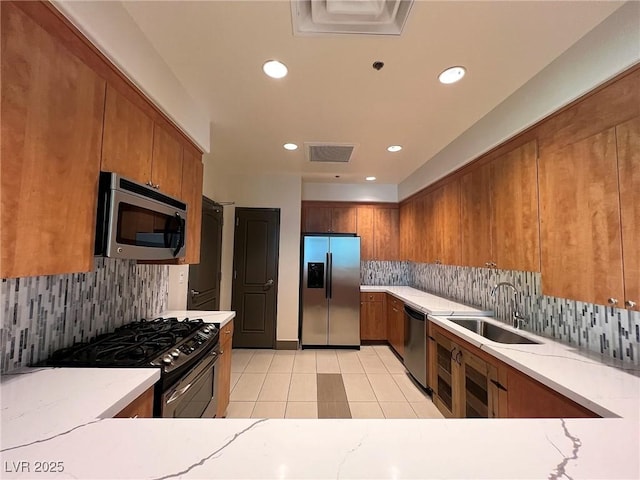 kitchen featuring brown cabinets, visible vents, appliances with stainless steel finishes, light tile patterned flooring, and a sink