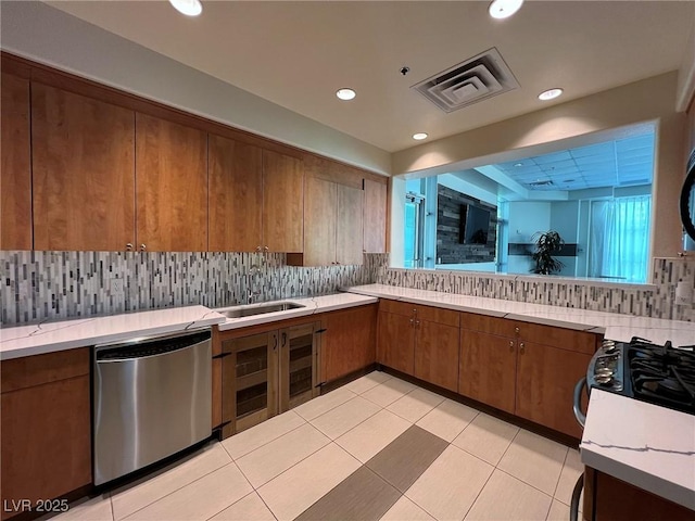 kitchen featuring a sink, visible vents, stainless steel dishwasher, decorative backsplash, and brown cabinetry