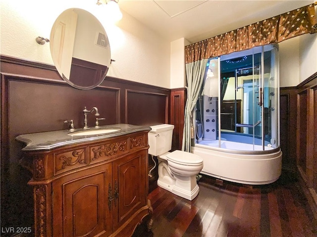 bathroom featuring a tub to relax in, visible vents, toilet, a wainscoted wall, and wood finished floors