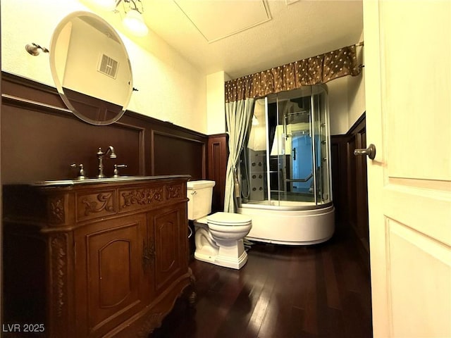 full bathroom with toilet, a decorative wall, a wainscoted wall, wood finished floors, and visible vents