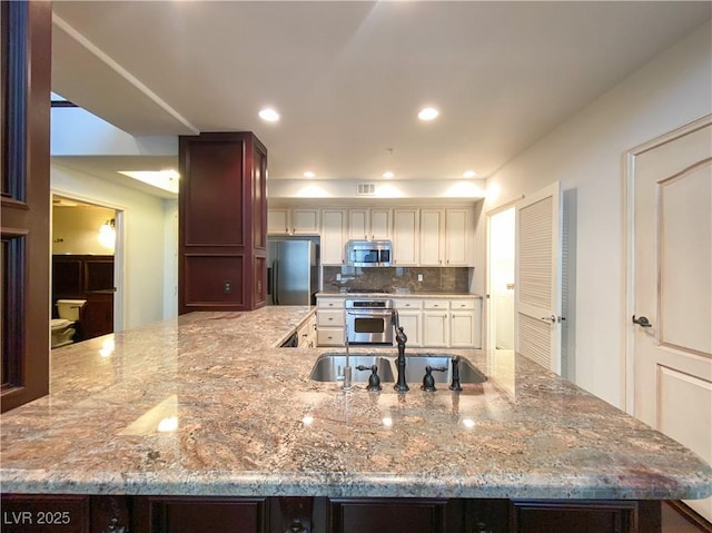 kitchen with tasteful backsplash, visible vents, light stone counters, stainless steel appliances, and a sink