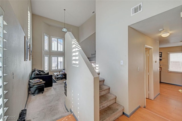 staircase with baseboards, a high ceiling, visible vents, and wood finished floors