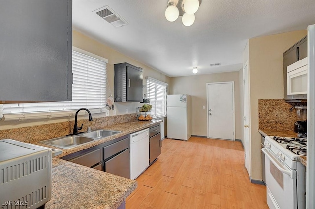 kitchen featuring white appliances, a sink, visible vents, light wood-style floors, and light countertops