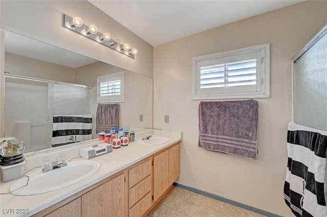 bathroom featuring double vanity, a shower stall, baseboards, and a sink