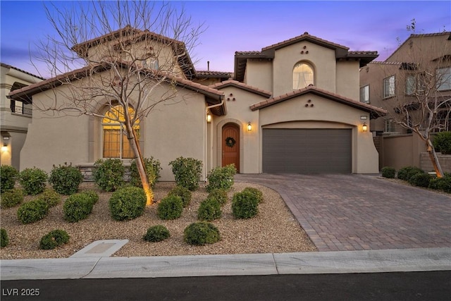 mediterranean / spanish-style home featuring a garage, decorative driveway, a tile roof, and stucco siding