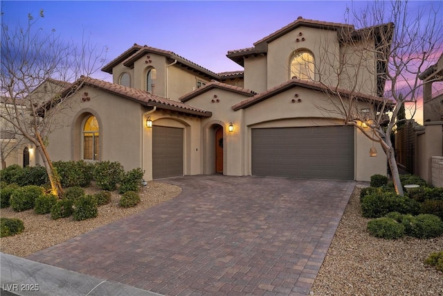 mediterranean / spanish-style home with decorative driveway, a tiled roof, and stucco siding