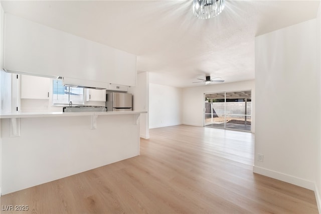 unfurnished living room with light wood-type flooring, a sink, baseboards, and ceiling fan with notable chandelier