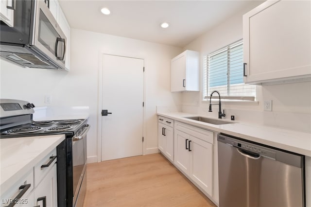 kitchen featuring light stone counters, stainless steel appliances, a sink, white cabinets, and light wood-type flooring