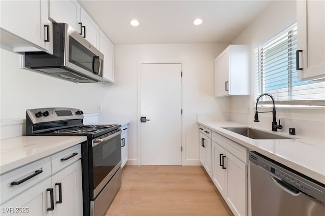 kitchen featuring light stone counters, white cabinetry, stainless steel appliances, and a sink