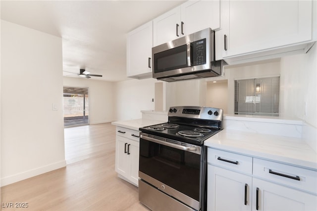 kitchen featuring light stone counters, a ceiling fan, white cabinets, appliances with stainless steel finishes, and light wood finished floors