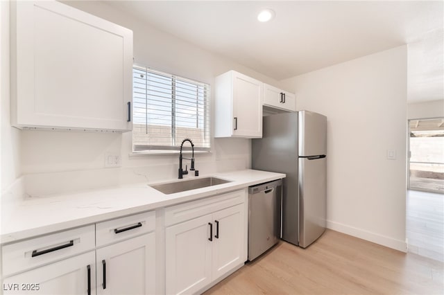 kitchen with baseboards, white cabinets, stainless steel appliances, light wood-style floors, and a sink