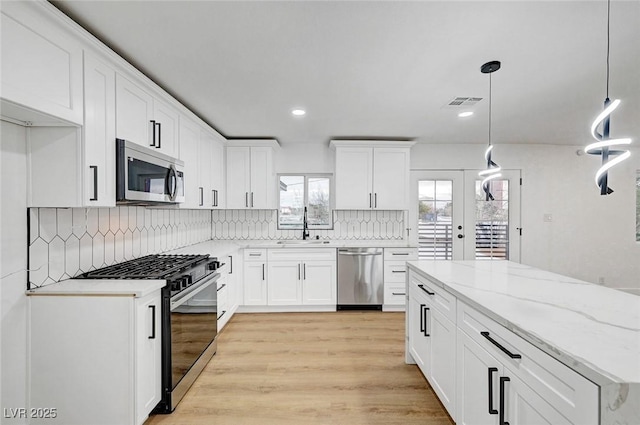 kitchen with tasteful backsplash, appliances with stainless steel finishes, light wood-type flooring, white cabinetry, and a sink