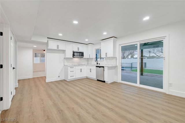 kitchen with stainless steel appliances, white cabinets, light wood finished floors, and tasteful backsplash