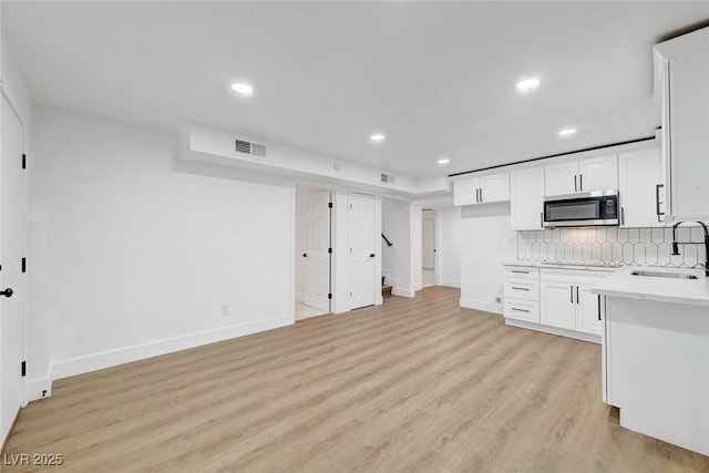 kitchen with a sink, visible vents, light wood-type flooring, tasteful backsplash, and stainless steel microwave