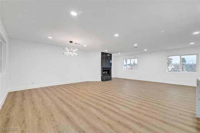 unfurnished living room with recessed lighting, a tiled fireplace, an inviting chandelier, light wood-style floors, and baseboards