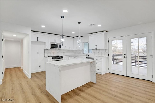 kitchen with range with gas stovetop, a center island, stainless steel microwave, visible vents, and a sink