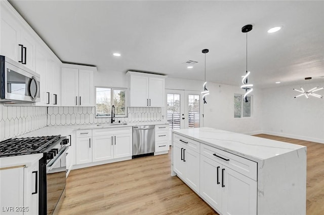 kitchen with decorative light fixtures, stainless steel appliances, decorative backsplash, light wood-style floors, and a sink