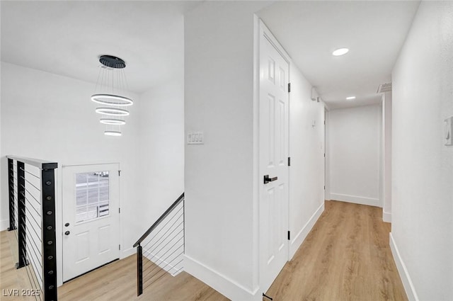 corridor featuring recessed lighting, light wood-style flooring, an inviting chandelier, an upstairs landing, and baseboards