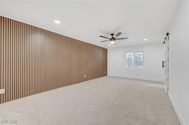 empty room featuring a barn door, wooden walls, light colored carpet, ceiling fan, and recessed lighting