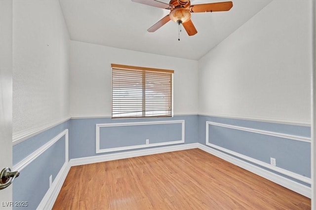 empty room with a wainscoted wall, wood finished floors, and a ceiling fan