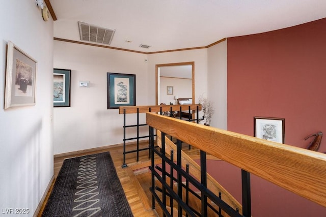 interior space with wood finished floors, an upstairs landing, baseboards, visible vents, and crown molding