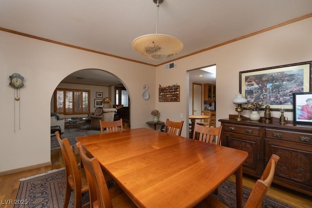 dining space with light wood-type flooring, visible vents, arched walkways, and ornamental molding