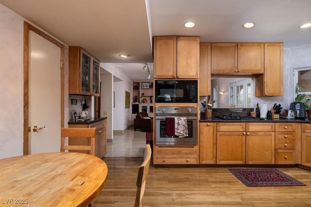 kitchen featuring gas stovetop, light wood-style floors, glass insert cabinets, black microwave, and oven