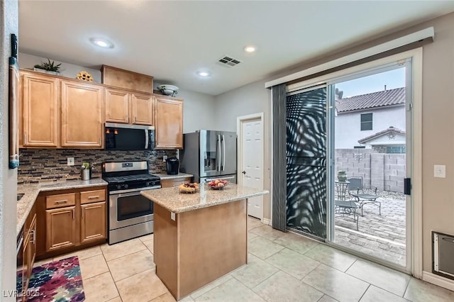 kitchen with light stone counters, stainless steel appliances, a kitchen island, visible vents, and tasteful backsplash