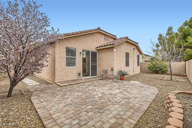 back of house featuring a tile roof, a fenced backyard, a patio, and stucco siding