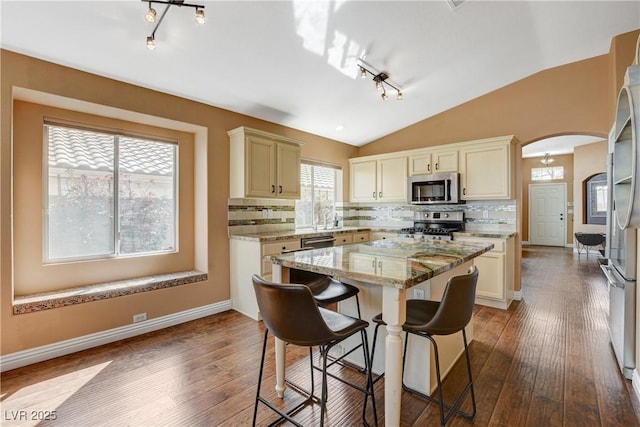 kitchen featuring arched walkways, lofted ceiling, a kitchen island, appliances with stainless steel finishes, and dark wood finished floors