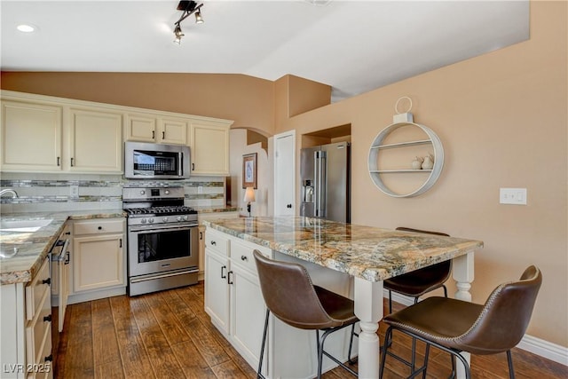 kitchen featuring lofted ceiling, dark wood-style flooring, a sink, stainless steel appliances, and backsplash