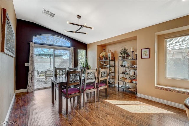 dining room with lofted ceiling, visible vents, an inviting chandelier, wood finished floors, and baseboards