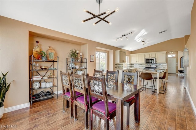 dining room with arched walkways, light wood finished floors, lofted ceiling, visible vents, and a chandelier