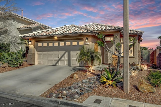 mediterranean / spanish-style home featuring driveway, an attached garage, a tile roof, and stucco siding