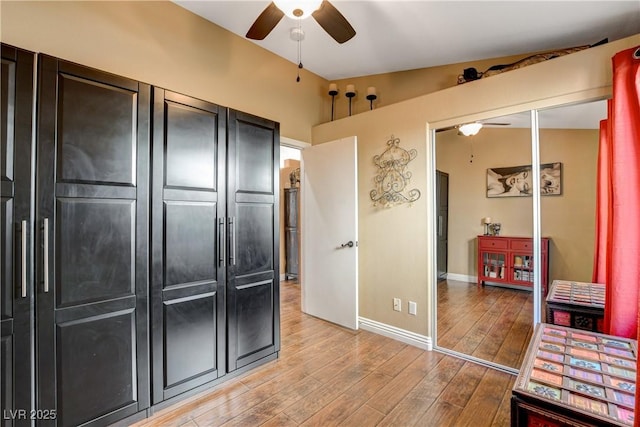 interior space with a ceiling fan, lofted ceiling, baseboards, and light wood finished floors