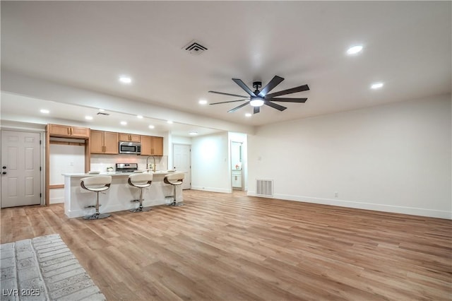 unfurnished living room with light wood-type flooring, visible vents, a sink, and ceiling fan