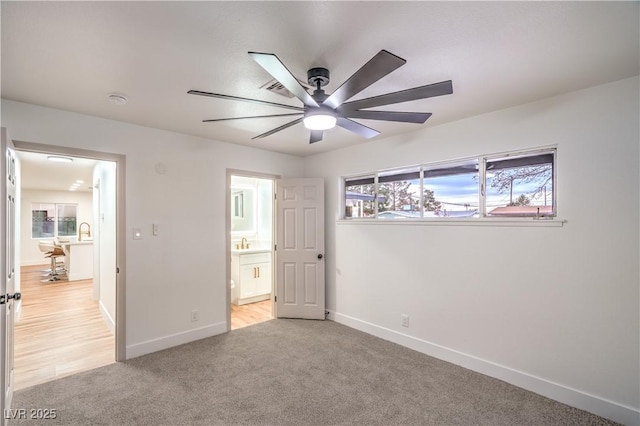 unfurnished bedroom featuring light carpet, ensuite bath, baseboards, and a ceiling fan