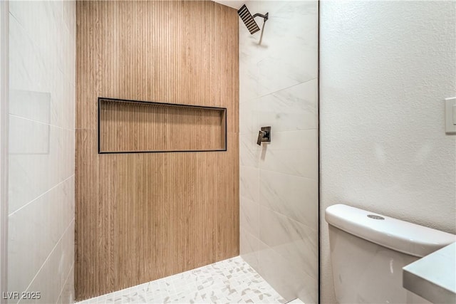 bathroom featuring a textured wall, tiled shower, and toilet