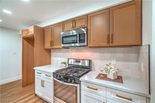 kitchen with light wood finished floors, baseboards, appliances with stainless steel finishes, light countertops, and backsplash