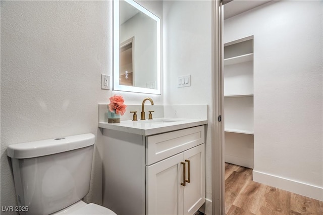 half bath with a textured wall, toilet, vanity, wood finished floors, and baseboards