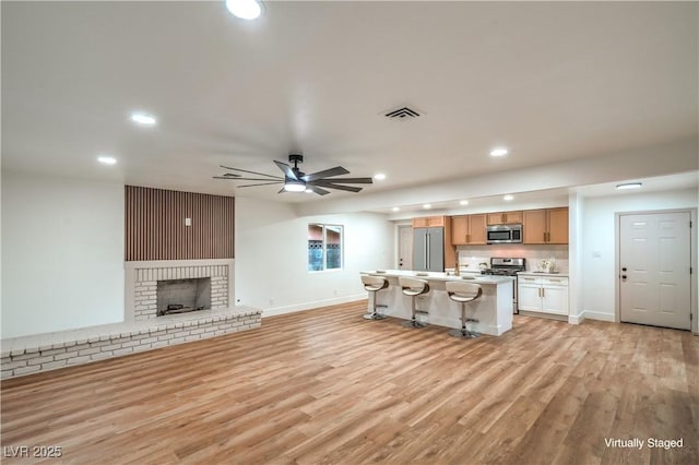 unfurnished living room with light wood-type flooring, visible vents, a fireplace, and ceiling fan