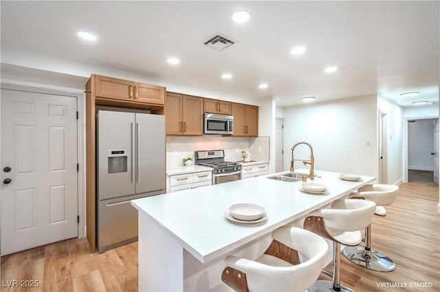 kitchen featuring a breakfast bar, a sink, visible vents, appliances with stainless steel finishes, and light wood finished floors