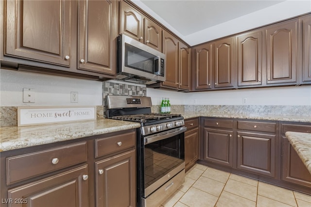 kitchen with light tile patterned floors, appliances with stainless steel finishes, light stone counters, and dark brown cabinets